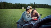 Young farmer couple looking at a laptop on pick-up truck hood while working on a farm