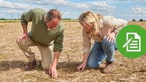 Two people examining soil in a field. 