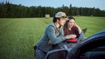 Una pareja de jóvenes agricultores mirando una computadora portátil en el capó de una camioneta mientras trabajaba en una granja