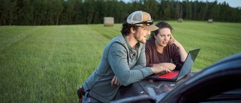 Young farmer couple looking at a laptop on pick-up truck hood while working on a farm