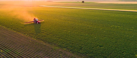 An aerial view of a tractor spraying a soybean field. An aerial view of a tractor spraying a soybean field.