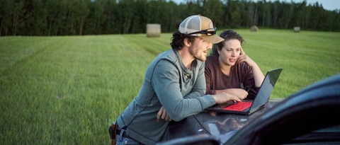 Una pareja de jóvenes agricultores mirando una computadora portátil en el capó de una camioneta mientras trabajaba en una granja