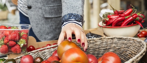 Close up of hand picking tomato from basket.