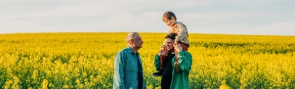 Father carrying son on shoulder next to grandfather in rapeseed field