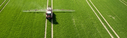 Aerial view of the tractor spraying the chemicals on the large green field