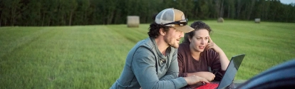 Young farmer couple looking at a laptop on pick-up truck hood while working on a farm