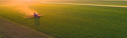 An aerial view of a tractor spraying a soybean field.