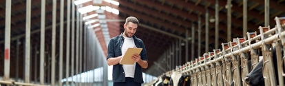 agriculture industry, farming, people and animal husbandry concept - happy smiling young man or farmer with clipboard and cows in cowshed on dairy farm; Shutterstock ID 562305472; Projekt-/Jobnummer: -