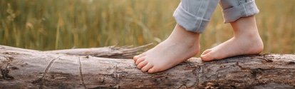 Child balancing on a trunk lying in front of a field
