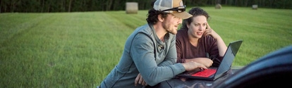 Una pareja de jóvenes agricultores mirando una computadora portátil en el capó de una camioneta mientras trabajaba en una granja
