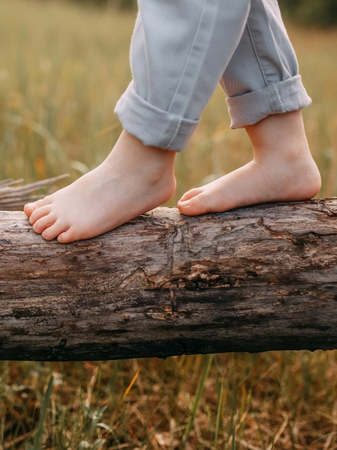 Child balancing on a trunk lying in front of a field