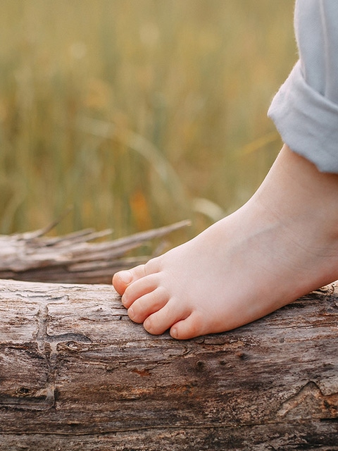 Child balancing on a trunk lying in front of a field