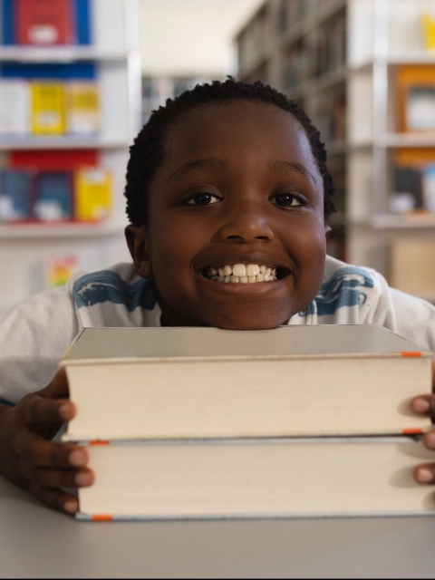 Happy schoolboy leaning his face on books and looking at camera