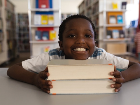 Happy schoolboy leaning his face on books and looking at camera